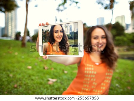 girl sitting in the park of Kuala Lumpur on the background of business centers and makes selfie, happy