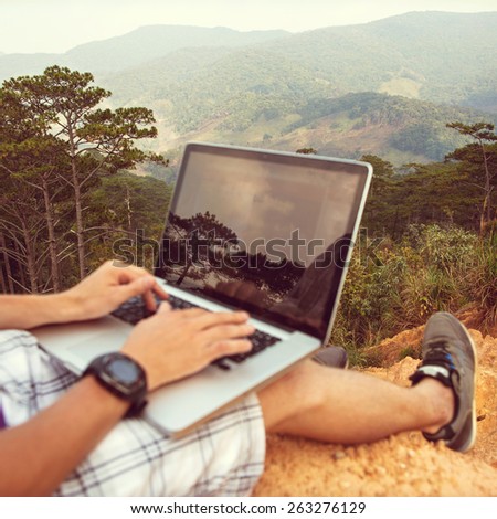man with laptop sitting on the edge of a mountain with stunning views of the valley