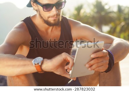 fashion guy sitting on the tablet, running in sunglasses on the beach with views of the mountains