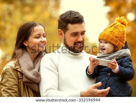 Family with a small daughter walk in autumn park with telephone