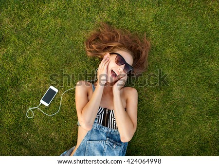 girl lying on the green grass, listening to music
