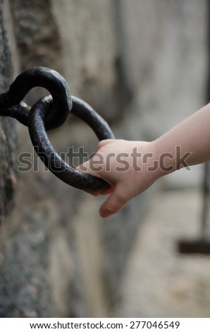 A child\'s hand holding on to a iron ring on a wall.