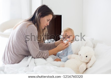 Mother and baby in pajamas, early in the morning, mom taking care of her sick toddler boy. Baby in bed with fever and running nose