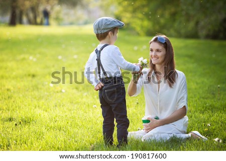 Beautiful kid and mom in spring park, flower and present. Mothers day celebration concept
