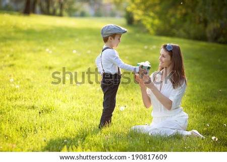 Beautiful kid and mom in spring park, flower and present. Mothers day celebration concept