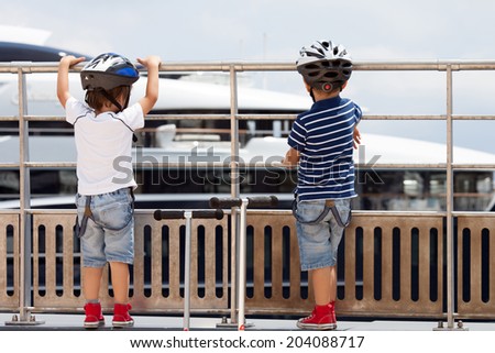 Two cute boys with scooters, looking at big boat on the port in Monaco
