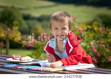 Adorable boy in red sweater, drawing a painting in a book, outdoor in the garden