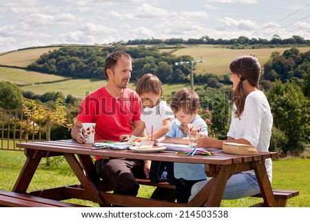 Happy family, sitting on a bench outdoor, drinking coffee and talking, kids reading a book