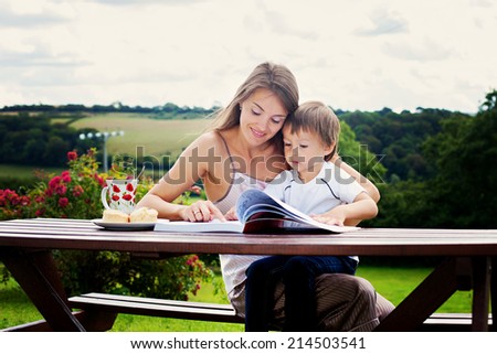 Mother and son, reading a book outdoor, summer day, eating sweet scones