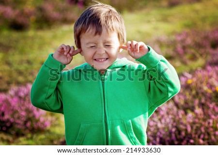 Small boy holds his hands over ears not to hear, making sweet funny face
