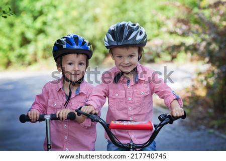 Portrait of two boys in the park, riding bike and scooter, smiling at the camera