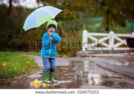 Little boy, jumping in muddy puddles in the park, rubber ducks in the puddle