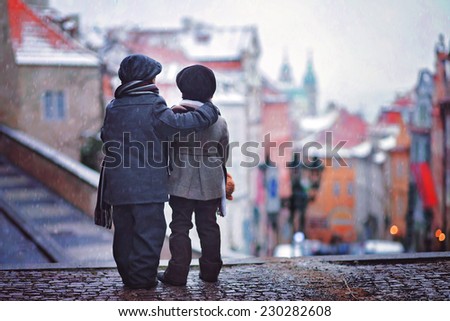 Two kids, standing on a stairs, backwards, view of Prague in front of them, snowy evening