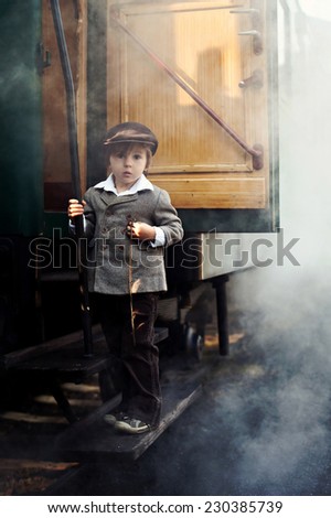 Boy, dressed in vintage coat and hat, standing on the stairs of steam train, holding pocket watch, steam behind him