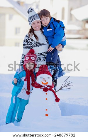 Happy beautiful family building snowman in garden, winter time, mom and two kids