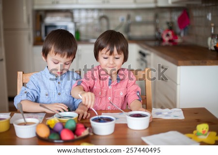 Two adorable boys, coloring eggs for Easter at home, having fun