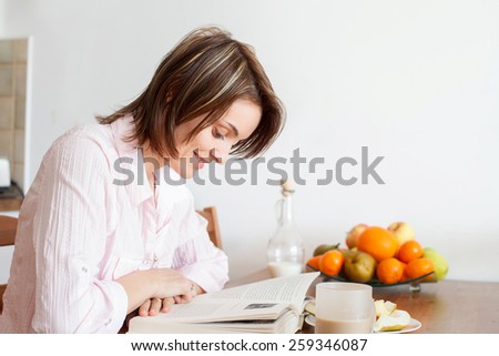 Young attractive woman, reading a book at home, eating fruits and drinking coffee