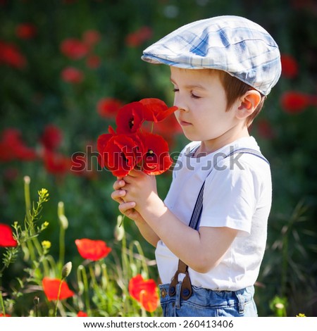 Cute little boy with poppy flower on poppy field on warm summer day, enjoying the day. Beautiful childhood, childish games