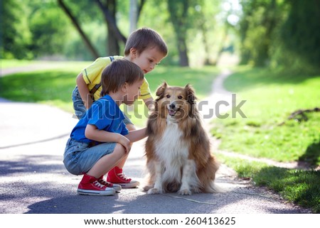 Two adorable boys, brothers, caressing cute dog in the park, summertime, enjoying the day