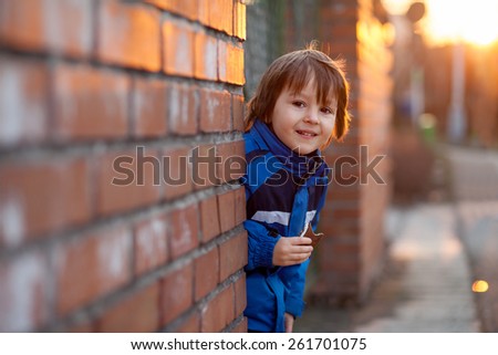 Adorable little boy, next to brick wall, eating chocolate bar on sunset, springtime