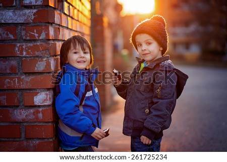 Two adorable little boys, next to brick wall, eating chocolate bar on sunset, springtime