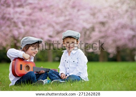 Two adorable caucasian boys in a blooming cherry tree garden, playing guitar in the afternoon