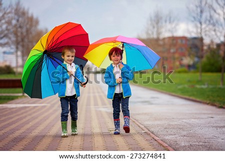 Two adorable little boys, walking in a park on a rainy day, playing and jumping, smiling, talking together, springtime