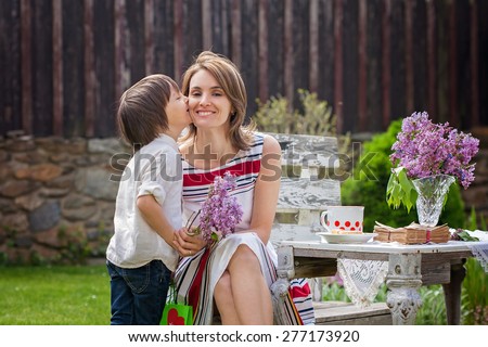 Beautiful mom, having coffee in a backyard, young cute child giving her present and flowers for her birthday. Mother day concept, love, happiness, cozy atmosphere