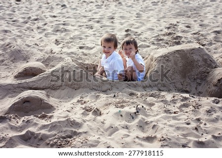 Adorable kids, playing on the beach, sitting in a ferrari car, made of sand, smiling at the camera, pretending to drive