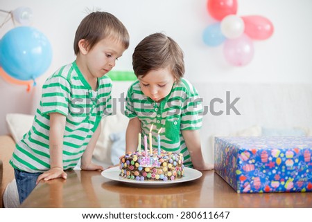 Beautiful adorable four year old boy and his brother in green shirts, celebrating his birthday, blowing candles on homemade baked cake, indoor. Birthday party for kids