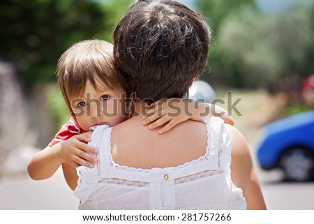 Grandmother, holding and hugging her grandson, little cute caucasian boy, outdoors, tender portrait