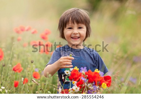Cute kid boy with poppy flowers and other wild flowers in poppy field on warm summer day, nice soft evening light