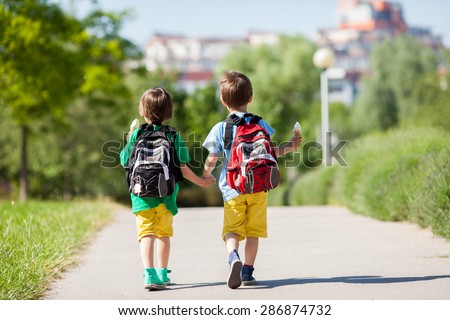 Two adorable boys in colorful clothes and backpacks, walking away, holding and eating ice cream on a sunny summer afternoon, warm day, casual clothing
