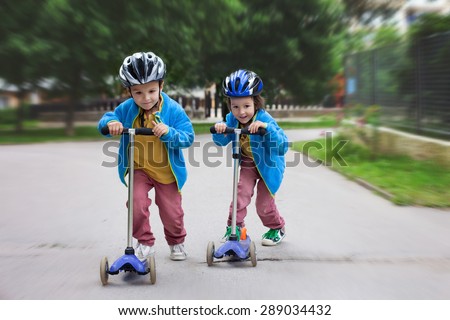 Two cute boys, compete in riding scooters, outdoor in the park, summertime