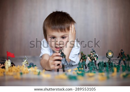 Cute little toddler boy, playing at home with soldiers and figurine toys, playing wars and peace