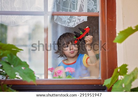 Sweet little boy, playing with airplane early in the morning on the window, view from outdoor through the window