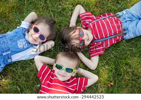 Happy cheerful smiling children, laying on a grass, wearing sunglasses, smiling at the camera, shot from above