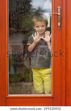 Little boy behind the window in the rain, looking sad