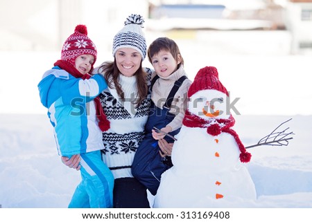 Happy beautiful family building snowman in garden, winter time, mom and two kids