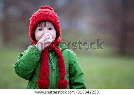 Little boy, sneezing and blowing his nose outdoor on a sunny winter day