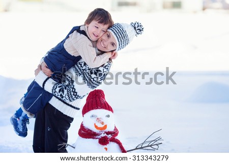 Happy beautiful family building snowman in garden, winter time, mom and kid