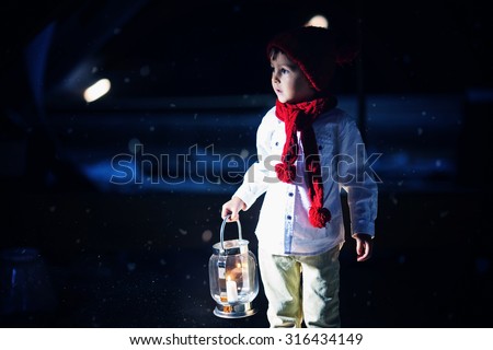 Sweet boy, holding a lantern, looking at a light coming through a window, standing in the snow