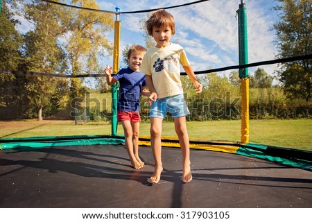 Two sweet kids, brothers, jumping on a trampoline, summertime, having fun. Active children