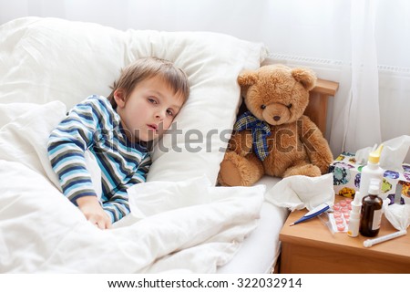 Sick child boy lying in bed with a fever, resting at home