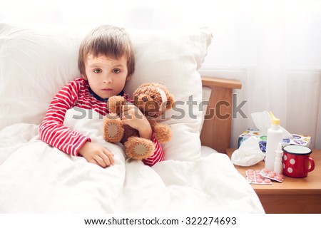 Sick child boy lying in bed with a fever, holding terry bear with band aid, resting