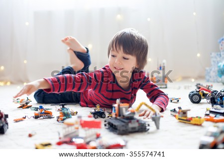 Little child playing with lots of colorful plastic toys indoor, building different cars and objects