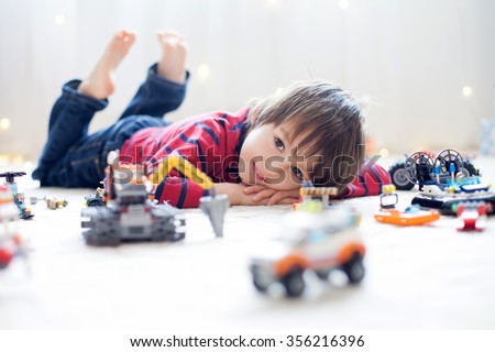 Little child playing with lots of colorful plastic toys indoor, building different cars and objects