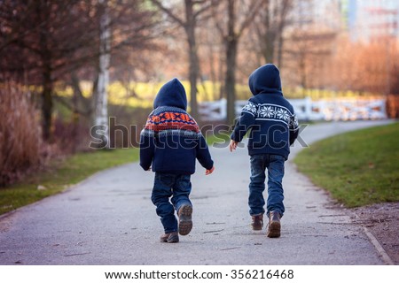 Two sweet boys running away on a footpath in the park on a sunny winter day, outdoors activity