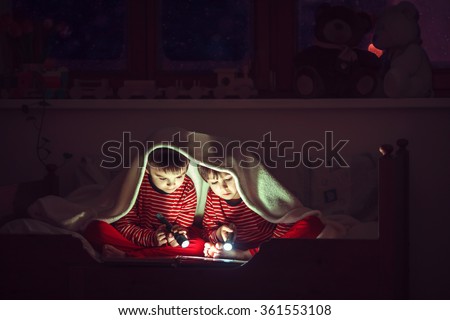 Two sweet boys, reading a book in bed after bedtime, using flashlights, winter night