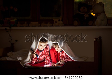 Two sweet boys, reading a book in bed after bedtime, using flashlights, winter night